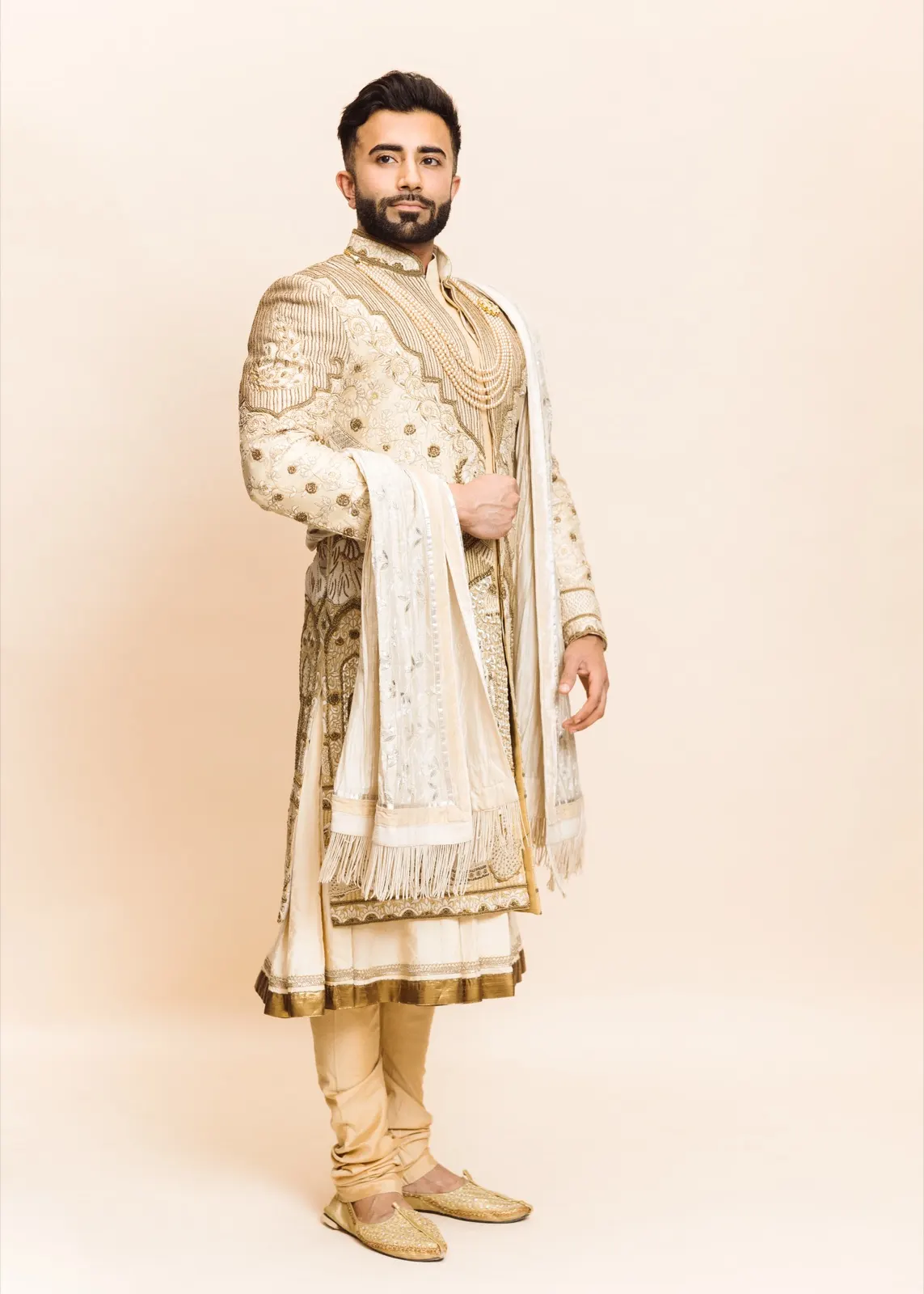 Hemel holds a composed full-length pose in an ornate cream sherwani with gold embroidery and pearls.