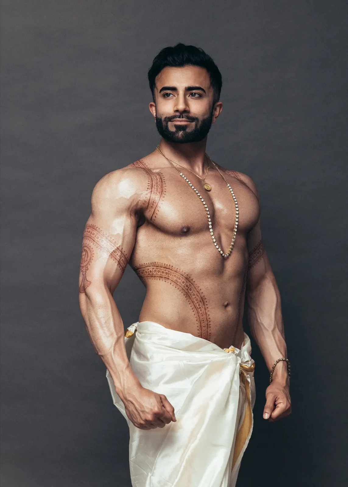 Hemel poses in a three-quarter portrait wearing an ivory dhoti, layered gold jewellery, and traditional body art.