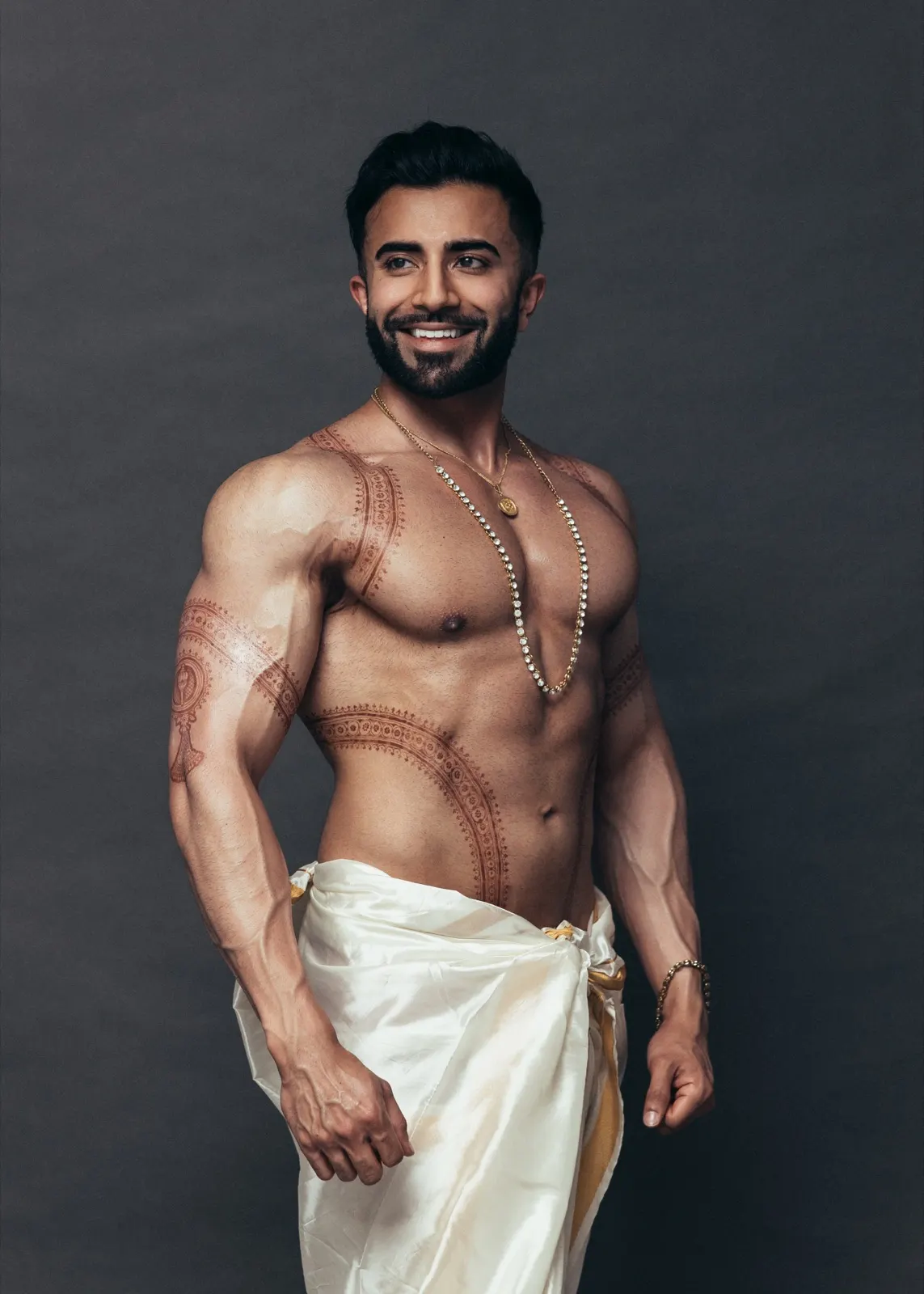 Hemel smiles in a three-quarter dhoti portrait featuring gold jewellery and intricate body art.