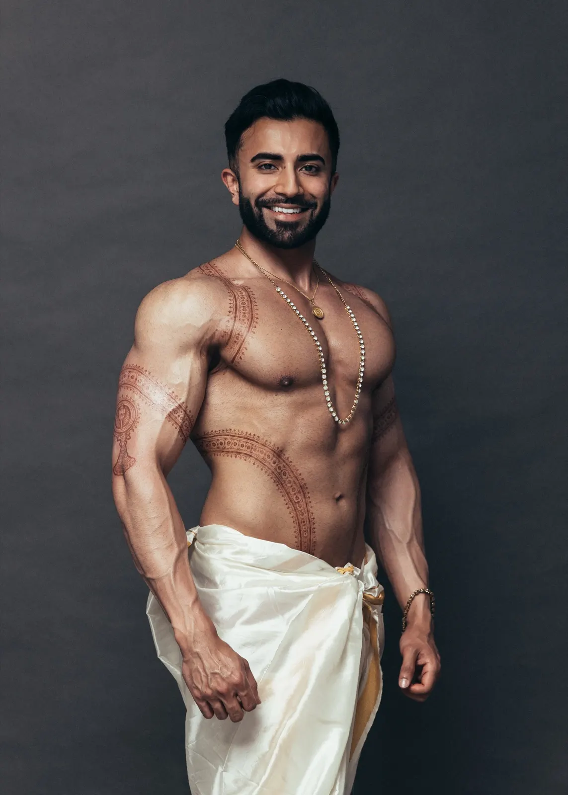 Hemel smiles confidently in an ivory dhoti with gold jewellery against a dark studio background.