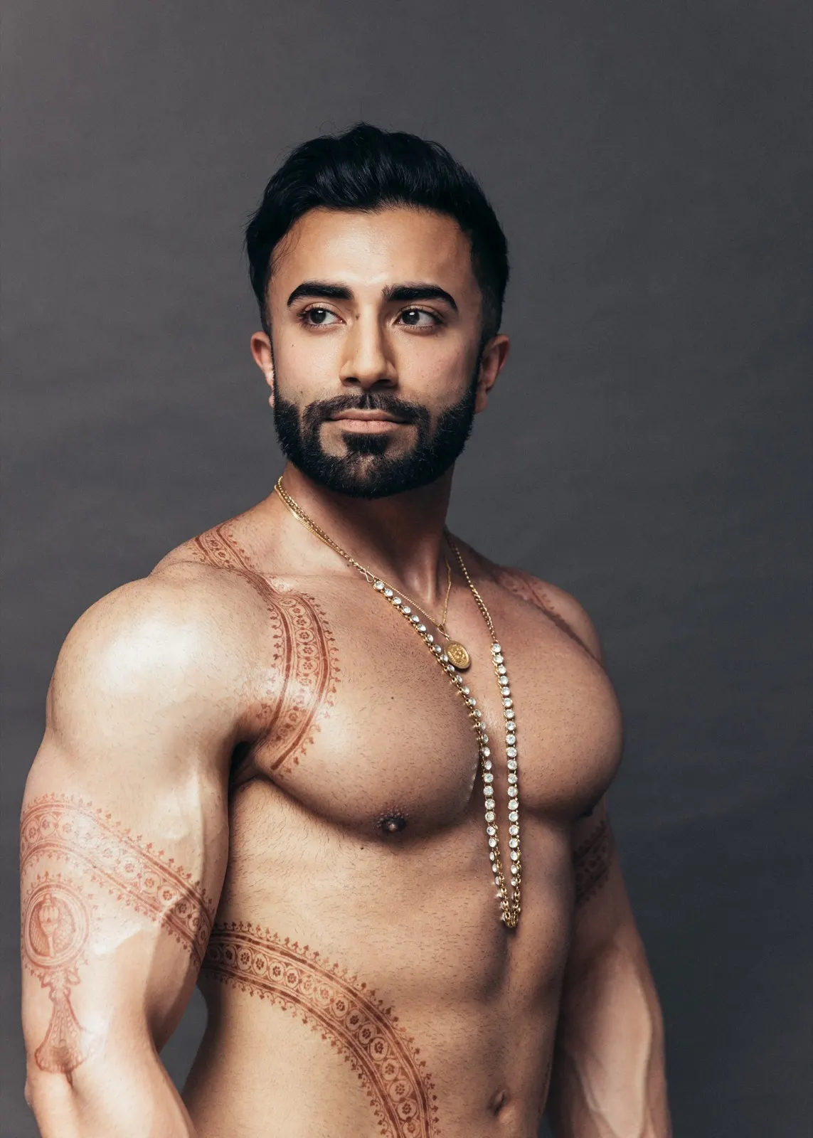 Hemel looks thoughtfully to the side in a close portrait highlighting his jewellery and detailed body art.