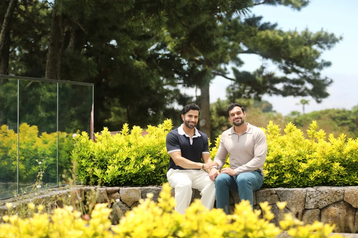 Hemel and Sundeep sitting together among yellow flowering shrubs in Jeju