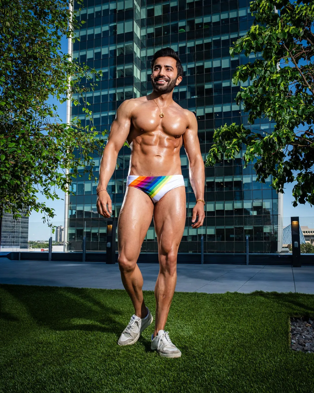 Hemel smiles while walking across a rooftop lawn in rainbow swim briefs and sneakers.
