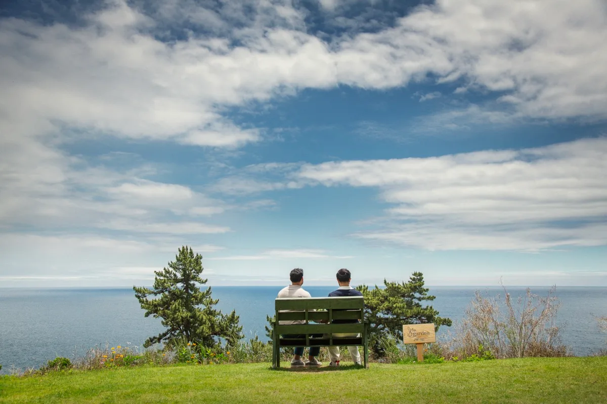 Hemel and Sundeep sitting on a bench overlooking the ocean in Jeju