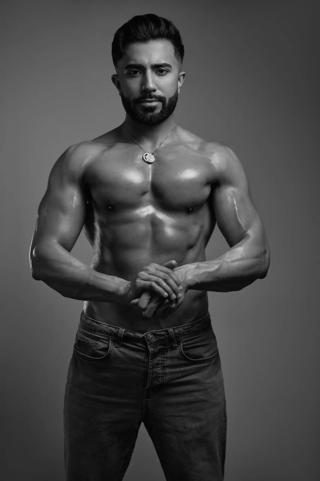 Hemel faces the camera in a black-and-white studio fitness portrait with clasped hands and a defined muscular build.